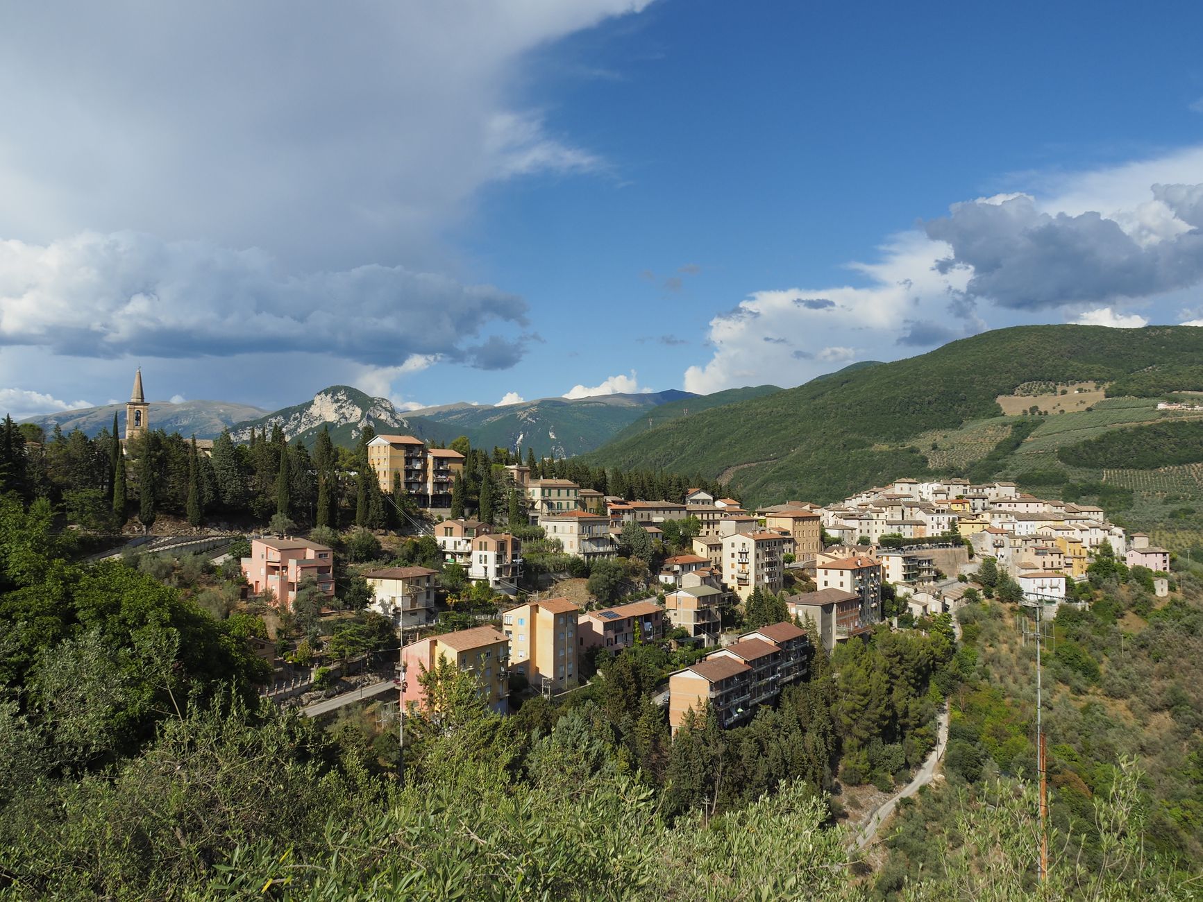 Picturesque view of an Italian hill town nestled among lush green hills under a vibrant sky.