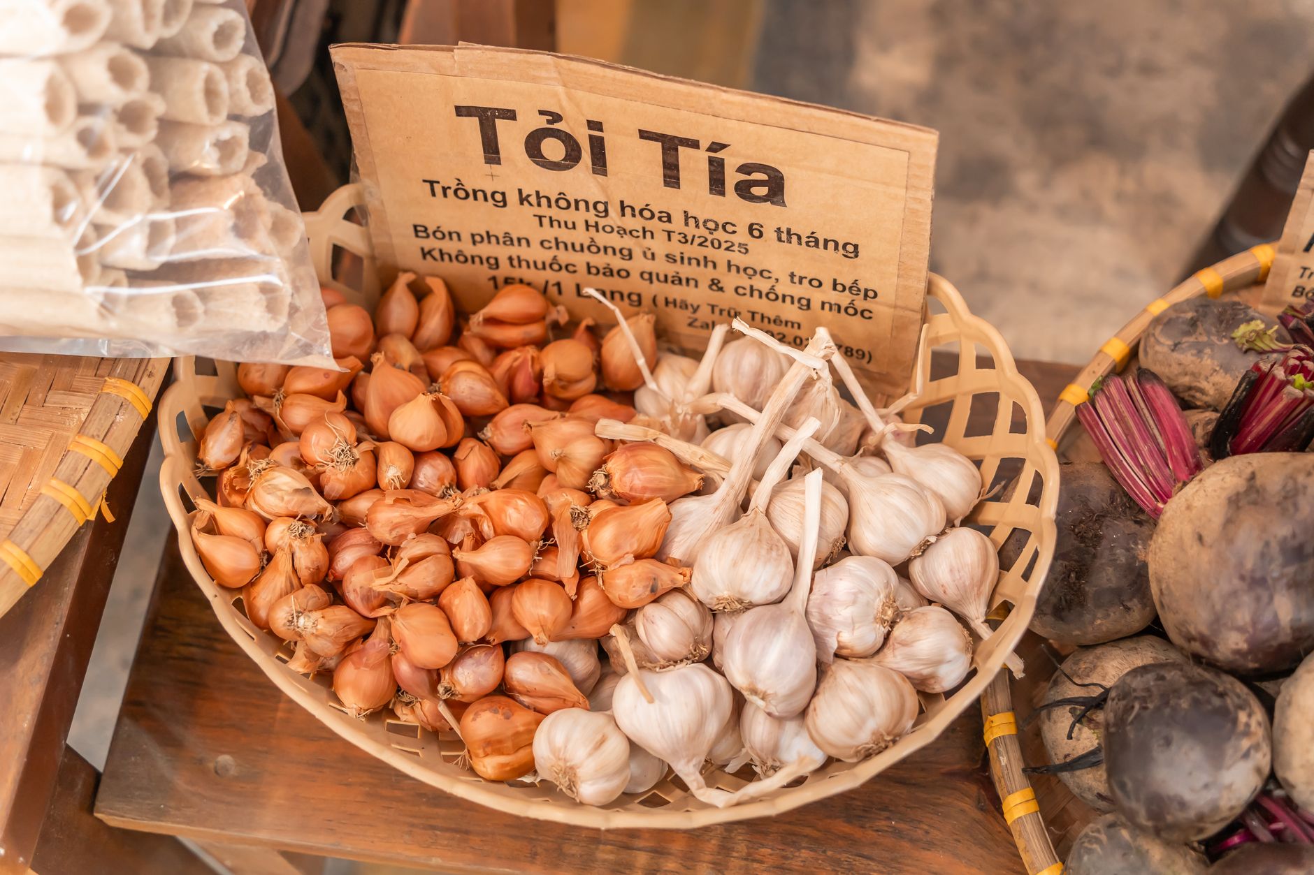 A basket of organic garlic and shallots on display at a market stall, showcasing fresh produce.
