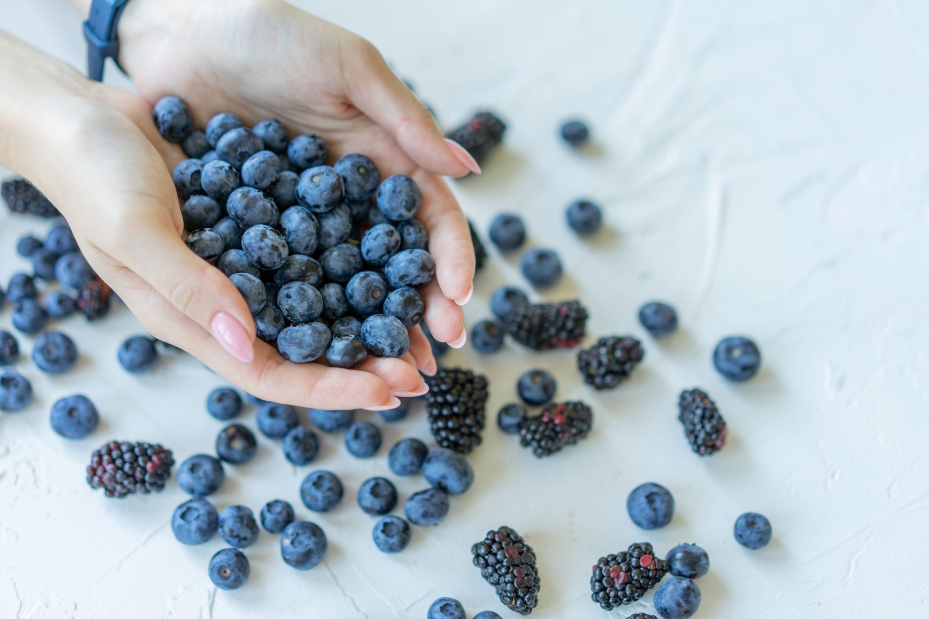 Close-up of hands holding fresh blueberries and blackberries on a light surface.