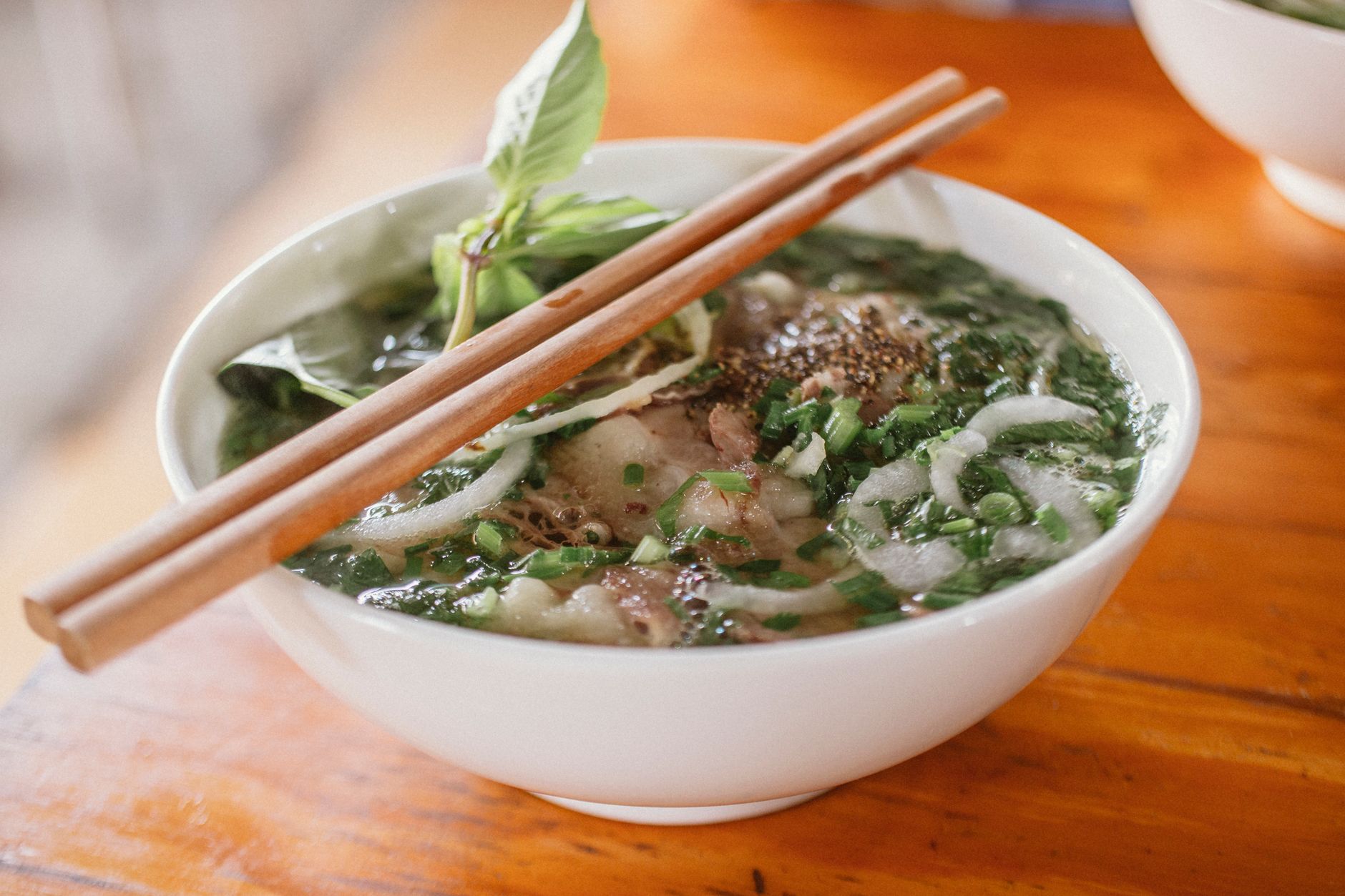 Delicious Vietnamese pho with fresh herbs and beef in a ceramic bowl, served with chopsticks.