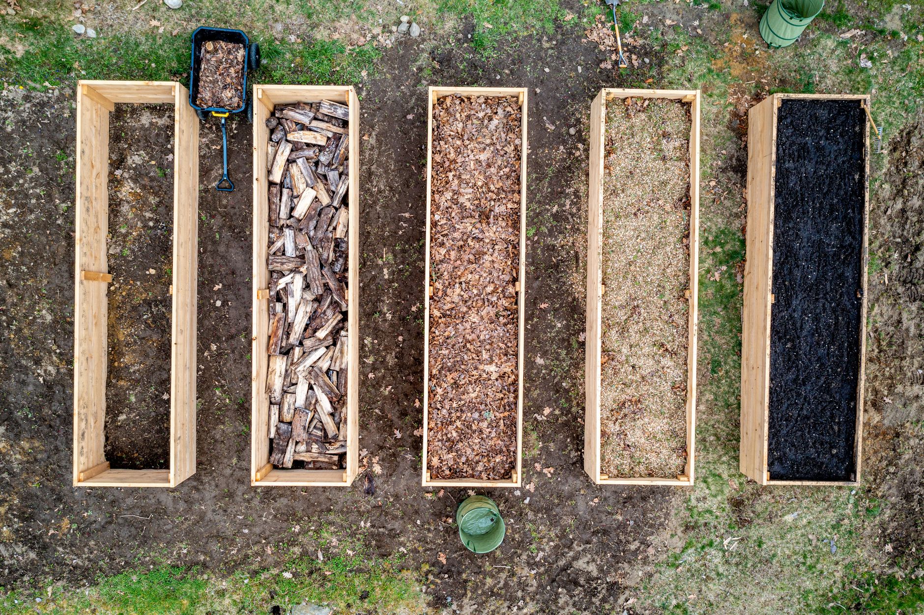 Top view of wooden boxes with piles of firewood wood chips sawdust and coal placed on ground in agricultural plantation